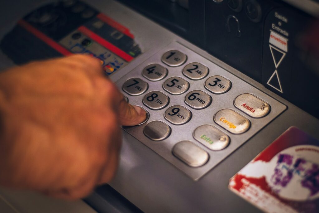 A mão de uma pessoa adulta apertando a tecla 0 de um caixa eletrônico.